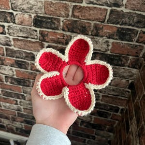 May include: A red crocheted flower hair scrunchie with a white border.