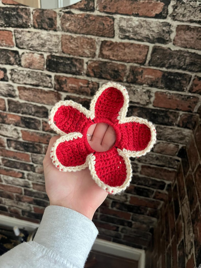 May include: A red crocheted flower hair scrunchie with a white border.