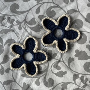 May include: Two crocheted flower hair scrunchies in navy blue with a white trim.