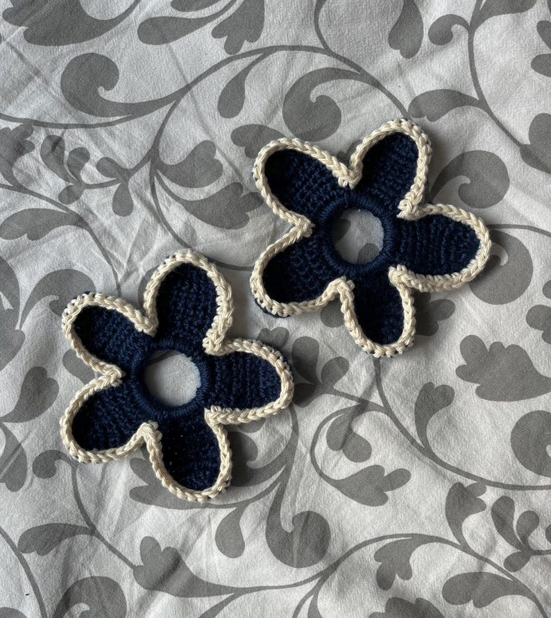 May include: Two crocheted flower hair scrunchies in navy blue with a white trim.