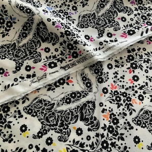 May include: White fabric featuring a repeating black skunk pattern filled with floral details. The design includes small black flowers and scattered accents in pink, orange, and yellow. The selvage edge displays the text Free Spirit Presents LINEWORK and PWTP155 Lil Stinker.