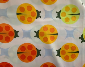 May include: A white fabric featuring a repeating pattern of stylized ladybugs in shades of orange, yellow, and lime green. Each ladybug has dark brown legs and a central line, with circular spots. Between the ladybugs are light blue four-pointed stars.