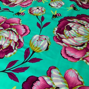 Op de afbeelding: Een levendige turquoise stof met een herhalend patroon van grote magenta en witte pioenrozen met donkerpaarse bladeren en stelen. Kleine gele en zwarte bijen zijn verspreid over het bloemmotief, wat een kleurrijke botanische print creëert.