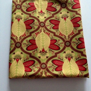 May include: A folded piece of fabric featuring a repeating damask-style pattern in shades of light green, deep red, and dark brown. The design consists of stylized, symmetrical floral motifs arranged within interconnected, curved geometric shapes.
