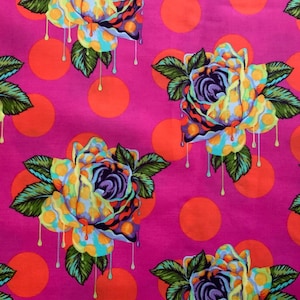 Op de afbeelding: Een levendige fuchsia stof met een herhalend patroon van gestileerde rozen met smeltende gele en blauwe bloemblaadjes, donkergroene bladeren en feloranje stippen verspreid over de achtergrond, wat zorgt voor een gedurfd en kleurrijk textielontwerp.
