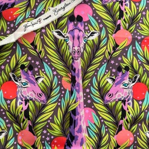 Op de afbeelding: Een stofprint met paarse en roze giraffen tussen groen gebladerte, kleine sterren en oranje cirkels op een donkerbruine achtergrond. Een witte zelfkant toont de tekst Everglow Tula Pink PWTP 203 Neck For Day.