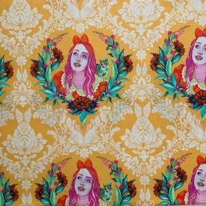 Op de afbeelding: Een gele stof met een herhalend patroon van een persoon met roze haar en een strik, omringd door een bloemenkrans en een kleine kat. De achtergrond bevat een wit damastontwerp met konijnen en bloemmotieven door de hele stof heen.