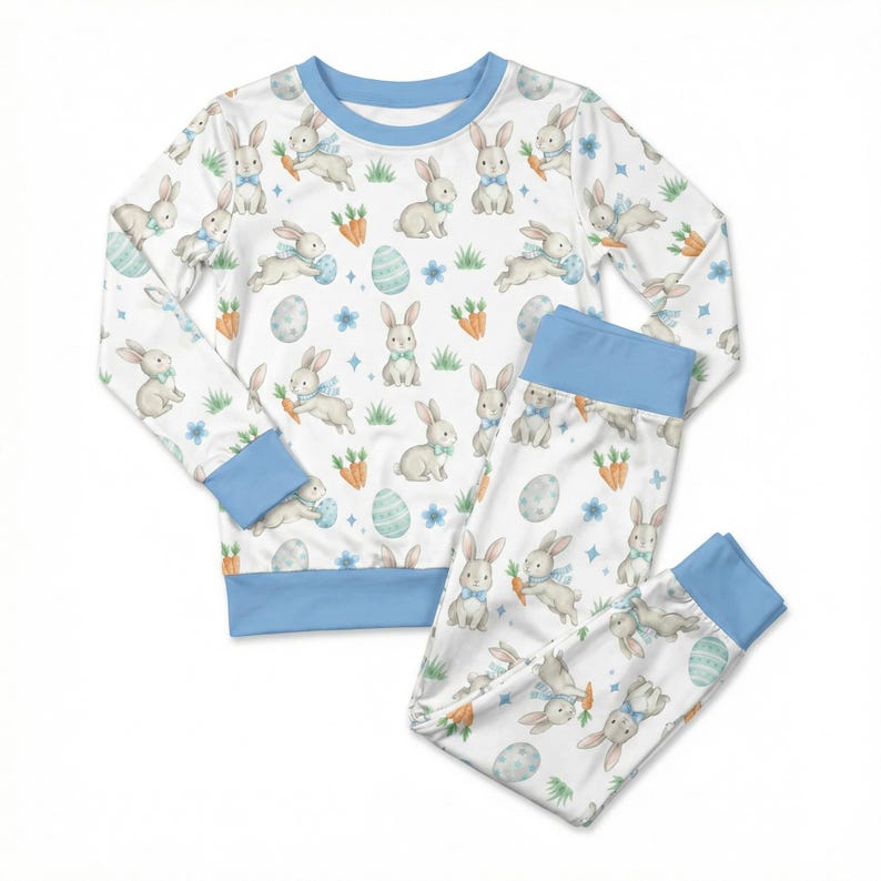 May include: White pajama set with a repeating pattern of bunnies, carrots, and Easter eggs. The long-sleeved top and pants have light blue trim. The bunny illustrations have blue bow ties.