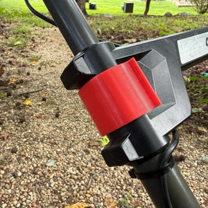 Pode incluir: Um conjunto de pega em plástico preto para corta-relvas com um grampo de bloqueio cilíndrico vermelho brilhante e uma etiqueta com o texto 40V LITHIUM. O componente liga-se a uma estrutura tubular e inclui um cabo preto fixado com braçadeira.
