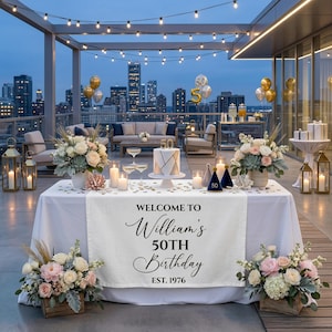 May include: A rooftop setting for a 50th birthday party, featuring a table adorned with flowers, candles, and a cake. A banner displays the message "Welcome to William's 50th Birthday, Est. 1976."
