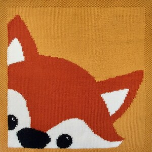 May include: A knitted orange fox peeking out from behind a yellow knitted background. The fox has white accents on its ears and around its eyes.