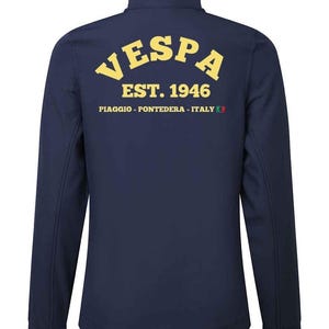 Könnte beinhalten: Marineblaue Jacke mit Reißverschluss und Stehkragen. Auf der Rückseite steht in Gelb das Wort "VESPA" in einem Bogen, darunter "EST. 1946" und "PIAGGIO - PONTEDERA - ITALY". Langärmlig.
