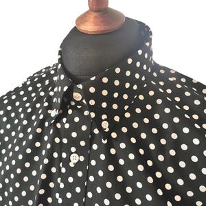 Könnte beinhalten: Ein schwarzes Hemd mit Knöpfen und weißem Punktmuster. Das Hemd hat einen Kragen und einen Knopfverschluss.