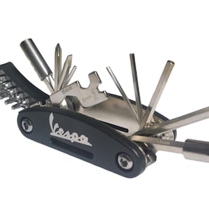Könnte beinhalten: Ein schwarzes Multitool mit dem aufgedruckten Wort "Vespa". Das Werkzeug verfügt über eine Vielzahl von Aufsätzen, darunter Schraubendreher, Schraubenschlüssel und einen Reifenheber.