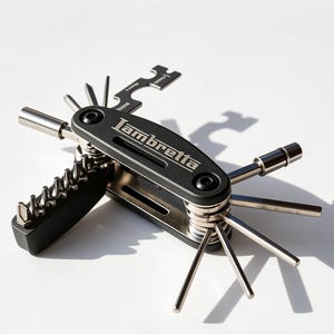 May include: A black multi-tool with the word Lambretta printed in white on the handle. The tool features various metallic attachments including hex keys, a screwdriver bit, and a wrench component, all extending from the central frame.