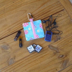 May include: A blue and pink zippered pouch with a ladybug print, a blue and black MP3 player, a set of black headphones, and three USB drives on a wooden surface.