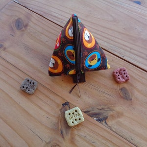 May include: A brown triangular zippered pouch with a dog print design. The pouch is open and the zipper is visible. There are three dog treats on a wooden surface.