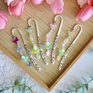 May include: Five silver bookmark pendants with floral designs and dangling charms. The charms include butterflies, beads, and teardrop-shaped stones in shades of green, blue, and pink.