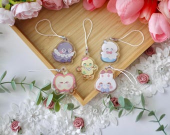 May include: A collection of five acrylic charms with cartoon animal designs, including an octopus, chick, snowman, apple, and bunny. Each charm has a white string for hanging. The charms are displayed on a wooden tray with floral decorations.
