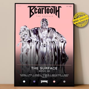 Puede incluir: Un póster enmarcado con el texto "Beartooth" y "The Surface" en negro. El póster presenta una figura metálica y reflectante sobre un fondo rosa. Las palabras "High Quality" están en una pegatina amarilla en la esquina superior derecha.