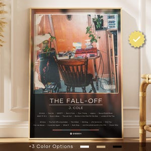 Op de afbeelding: Een ingelijste poster met de albumhoes van "The Fall-Off" van J. Cole. De afbeelding toont een kamer met een bureau, stoel en planten. De poster bevat de albumtitel, artiestennaam en tracklist. De lijst is goudkleurig.