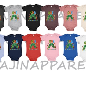 May include: A collection of baby onesies in various colors, each featuring a colorful graphic of a caterpillar and the word "ONE". The text "The Very Hungry Caterpillar" is also printed on the onesies. The brand name "TAJINAPPAREL" is printed at the bottom.