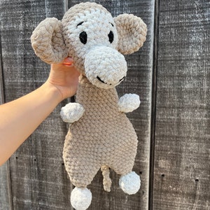 May include: A crocheted monkey toy with brown and white fur. The monkey has large, black eyes and a small, brown nose. The toy has white pom-poms on its feet.