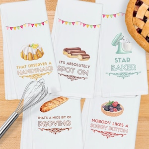 May include: Set of four white kitchen towels with colorful illustrations and baking puns. The towels feature a bundt cake, eclairs, a stand mixer, a baguette, and a tart. The text on the towels reads: "That deserves a handshake", "It's absolutely spot on", "Star Baker", "That's a nice bit of proving", and "Nobody likes a soggy bottom".