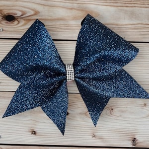 May include: A large navy blue glitter cheer bow with a silver rhinestone center.