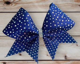 May include: A large navy blue cheer bow with iridescent rhinestones. The bow is made of glitter fabric and has a center piece of rhinestones.