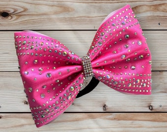 May include: A large pink bow with a black elastic band. The bow is covered in iridescent rhinestones.