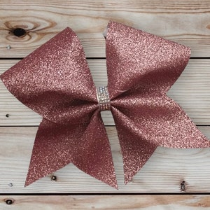 May include: A large rose gold glitter cheer bow with a clear rhinestone center.