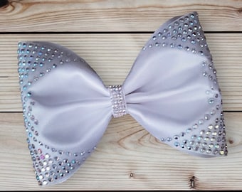 May include: A large white satin bow with a center band of iridescent rhinestones. The bow is decorated with a border of iridescent rhinestones.