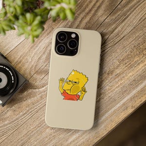 Puede incluir: Una funda de teléfono beige con una imagen de dibujos animados de un personaje amarillo con una camiseta roja y cabello negro. El personaje está haciendo un gesto con ambas manos.