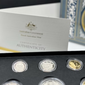Könnte beinhalten: Ein Satz australischer Münzen in einer schwarzen Präsentationsbox, mit einem Echtheitszertifikat im Hintergrund. Die Münzen sind silber- und goldfarben, und das Zertifikat ist weiß mit goldenem Text und dem australischen Regierungssiegel.
