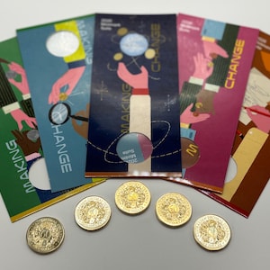 Puede incluir: Una colección de folletos coloridos con las palabras "MAKING CHANGE" y "CHANGE" impresas, junto con monedas de oro. Los folletos presentan ilustraciones de manos interactuando con monedas y otros objetos. Las monedas son de color dorado y tienen diseños intrincados.