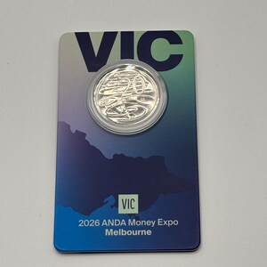 May include: A silver coin with a 20 denomination, in a clear plastic holder, is on a blue and green card. The card has the word "VIC" at the top and the text "2026 ANDA Money Expo Melbourne" at the bottom. The coin is a collectible item.