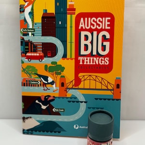 Puede incluir: Juego de cajas coleccionables Aussie Big Things con un recipiente cilíndrico a juego. La caja presenta ilustraciones de monumentos y animales australianos, con el texto "AUSSIE BIG THINGS". El recipiente tiene el texto "AUSSIE BIG" en rojo y blanco.