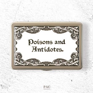 Peut inclure: Un boîtier métallique rectangulaire de couleur argentée avec un panneau central blanc portant le texte noir "Poisons and Antidotes." Le motif est encadré par une bordure en filigrane sombre et complexe. La marque "PAC Designs" est imprimée en dessous.