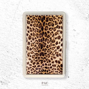 May include: A rectangular metal cigarette case featuring a prominent leopard print pattern in shades of brown, tan, and black. The case has a smooth, light-coloured border and the text PAC Designs is printed in small black letters at the bottom.