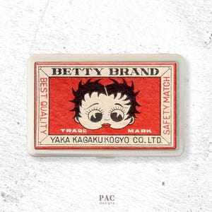 Könnte beinhalten: Eine weiße Keramik-Tasse mit schwarzem Henkel und dem Text "But First, Coffee" in schwarzer, handschriftlicher Schrift. Die Tasse steht auf einer weißen Oberfläche.