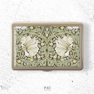 May include: A rectangular metal case with a gold-toned frame featuring a repeating botanical pattern of large cream-colored flowers, sage green leaves, and small yellow blossoms. The design is symmetrical, and the text PAC Designs is printed below.