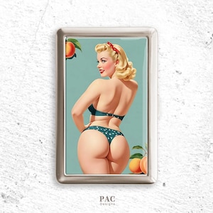 May include: A silver metal cigarette case featuring a retro pin-up girl illustration. The artwork depicts a woman in a teal bikini with white polka dots, peaches, and a red bow. The case has the text "PAC Designs" at the bottom.