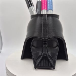 May include: Black plastic Darth Vader head shaped desk organizer with four pens inside.