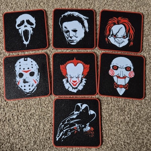 May include: Set of seven square coasters featuring iconic horror movie characters. Each coaster has a black background with a red border and a white and red graphic of a horror character, including Michael Myers, Pennywise, and Jason Voorhees.