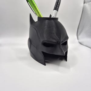 May include: Black Batman-shaped desk organiser with two pens inside. The pen on the left is green and has the text "TOO BUSY FOR BULLSHIT" on it. The pen on the right is black.
