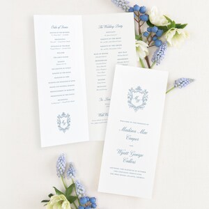 May include: A white wedding program with blue text and a decorative crest. The front cover displays the names Madison Mae Cooper and Wyatt George Collins, while the interior lists the order of service and wedding party members in a formal font.