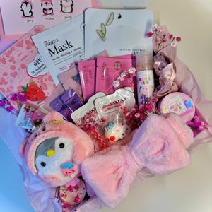 Könnte beinhalten: Eine rosa Geschenkbox mit Schönheitsprodukten, darunter Gesichtsmasken, ein Plüschpinguin, ein schleifenförmiges Stirnband und eine Sprühflasche. Die Box enthält auch eine Karte mit Pinguin-Illustrationen und dem Text "Just a little thing to say."