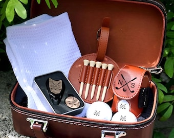 May include: A brown leather golf gift set with a handle, containing a white towel, golf balls, tees, and a small pouch. The set includes a metal tin with golf ball markers and a leather tee holder. The golf balls and pouch are branded with "N S" and crossed golf clubs.