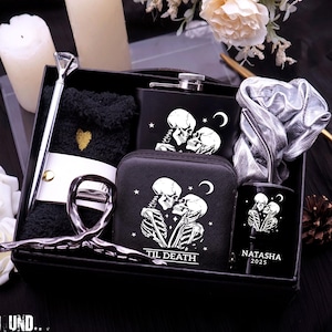 May include: A black gift set with a variety of items, including a flask, wallet, and tumbler, all featuring a skeleton couple design. The set also includes a pen, socks, and a hair accessory. The tumbler is personalized with the name "Natasha" and the year "2025".